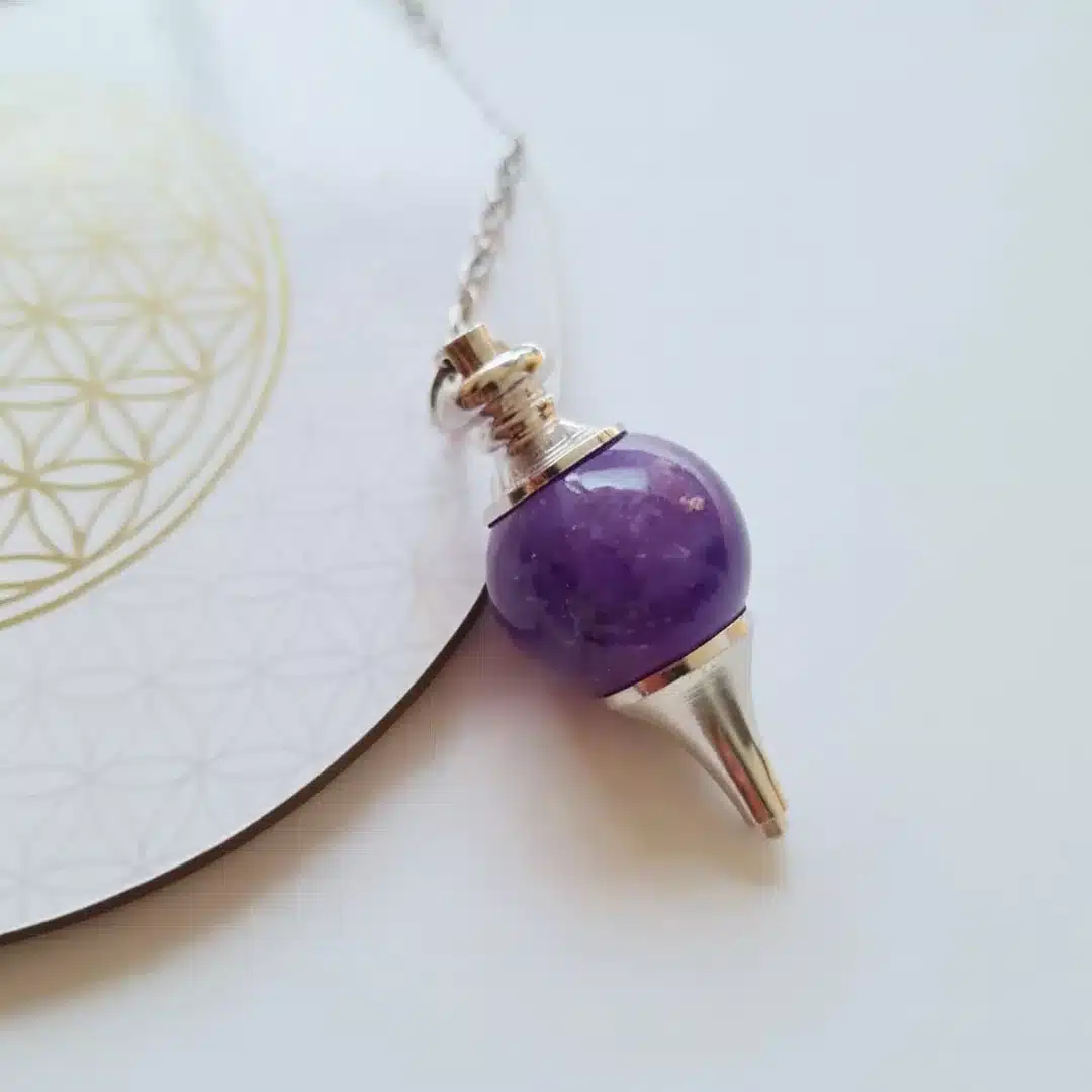 Pendule Séphoroton en améthyste posé sur une carte Fleur de Vie dorée – divination, intuition et harmonisation énergétique.