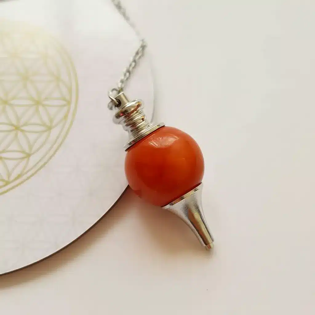 Pendule divinatoire Séphoroton en cornaline naturelle posé sur une carte Fleur de Vie dorée, ambiance spirituelle, minimaliste et lumineuse.